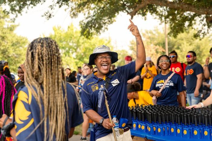 Group of students participating in Lion Walk. A student is shown holding a walking stick and waving.